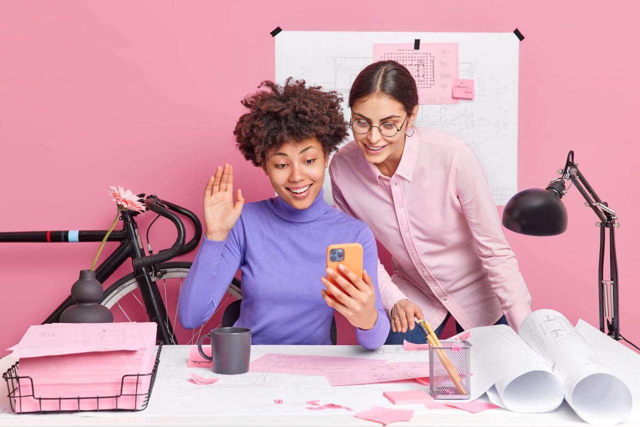 Two women collaborating happily over a phone in a creative workspace.