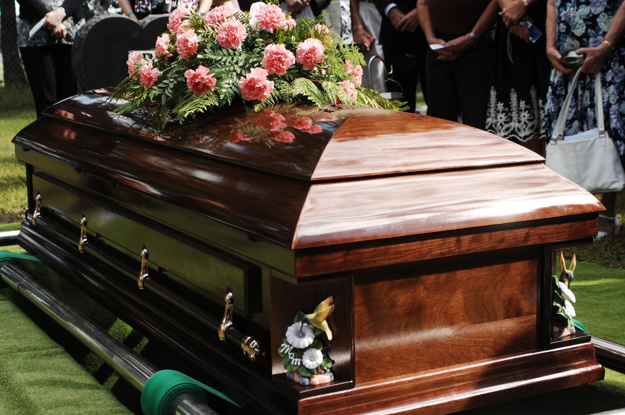 A wooden coffin adorned with pink flowers at a funeral.