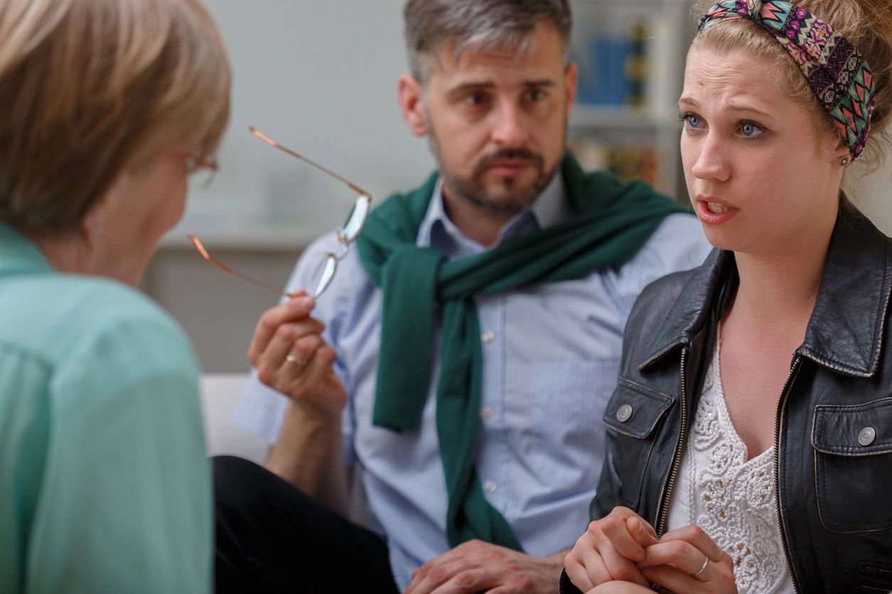 Three people engaged in a serious conversation indoors.